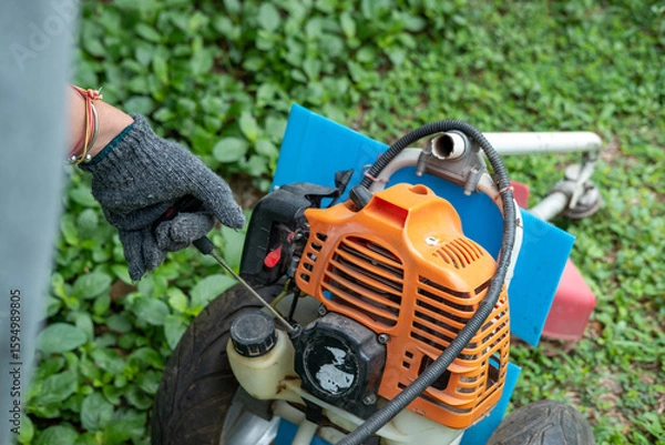 Obraz gardener pulling lawnmower starter cord, beginning the task of cutting the well-kept lawn