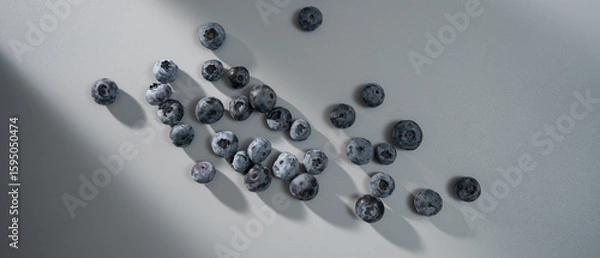 Fototapeta Fresh blueberries scattered on a light surface creating intriguing shadows in soft afternoon light