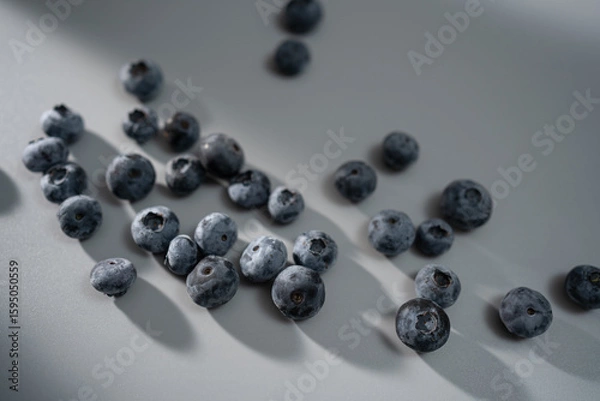 Fototapeta Fresh blueberries scattered on a surface casting soft shadows in natural light