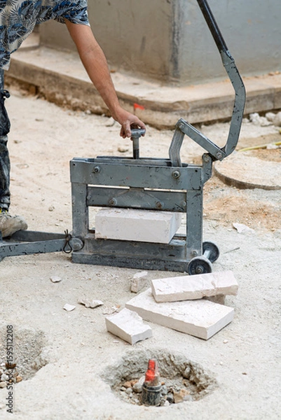 Obraz Worker operating a stone cutting machine on sandy ground—capturing manual craftsmanship and industrial technique at a construction site.