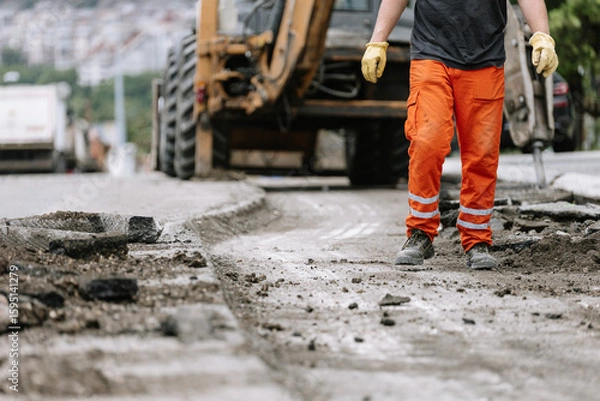 Obraz Construction worker repairs the street in urban area during daylight hours with heavy machinery nearby