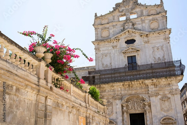 Fototapeta  Historic building with ornate architecture and vibrant flowers in pots against a clear blue sky