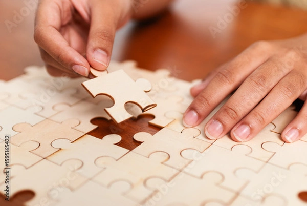 Fototapeta Solving the puzzle hands placing last piece indoor setting close-up focus on craft and patience
