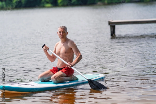 Fototapeta A man on a SUP board floats across a lake.