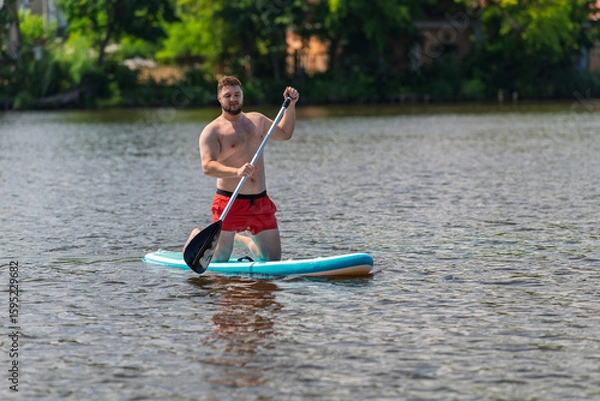 Fototapeta On a lake, a man of 30 years is floating on a SUP board.
