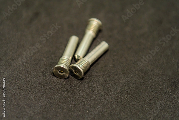 Fototapeta Three arranged metal screws on a dark background surface
