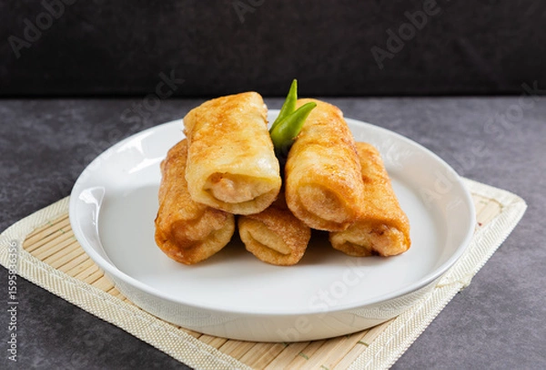 Obraz Sosis Solo (Sausage Solo). Special designation for a chicken dish wrapped in an omelet and shape like sausagea. Traditional Indonesian meat snack, served on a white plate with green chili garnish.