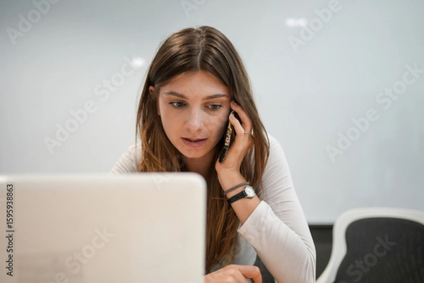 Fototapeta Stressed Businesswoman Talking on Phone While Working on Computer