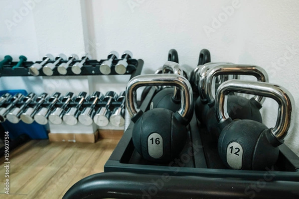 Fototapeta A row of dumbbells and a kettlebell are on a rack. The dumbbells are in various sizes and the kettlebell is black