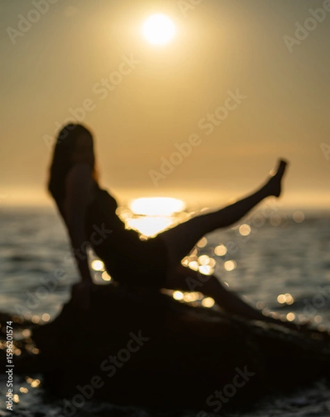 Fototapeta Silhouette of person sitting on rock near sea with leg raised during sunrise. Relaxation and summer vacation concept for design and poster