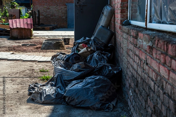 Obraz Black trash bags are stacked against a weathered brick wall, showing neglect in an empty industrial space under bright sunlight