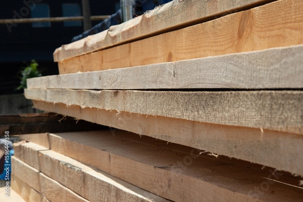 Obraz Sunlight illuminates neatly stacked wooden planks at a construction site, showcasing the texture and grain of the wood in clear detail