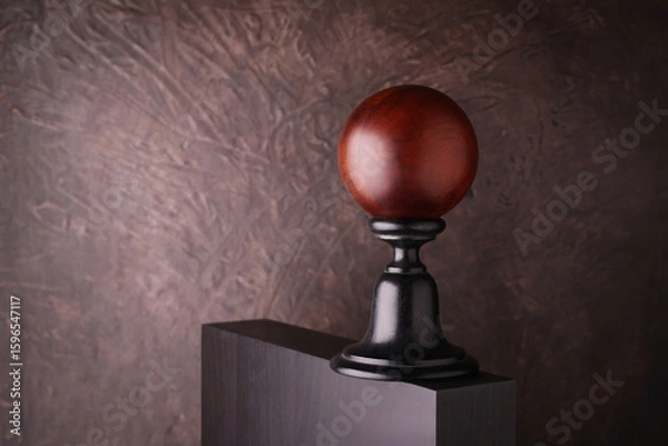 Fototapeta Sfera decorativa in legno su piedistallo nero con sfondo materico marrone