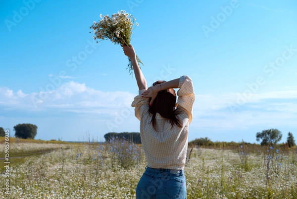 Obraz Young woman smiling while smelling daisies in field. Concept of peace and contentment. Summer bliss forever captured in this frame.