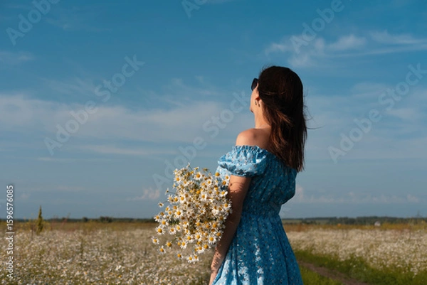 Obraz Young woman smiling while smelling daisies in field. Concept of peace and contentment. Summer bliss forever captured in this frame.