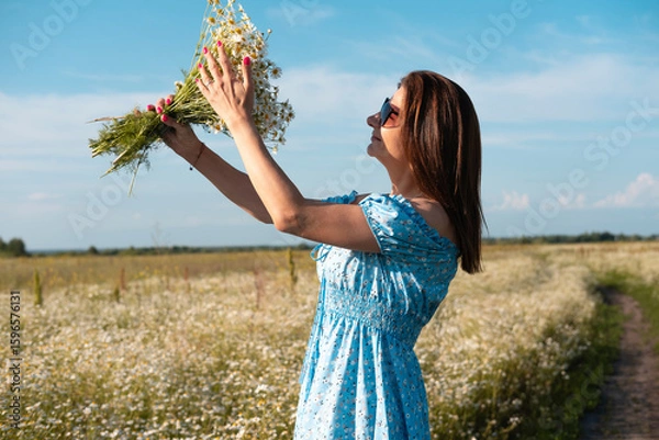 Obraz Young woman smiling while smelling daisies in field. Concept of peace and contentment. Summer bliss forever captured in this frame.