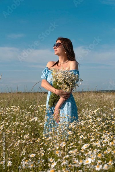 Obraz Young woman smiling while smelling daisies in field. Concept of peace and contentment. Summer bliss forever captured in this frame. vertical