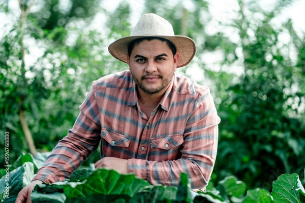 Fototapeta Young Latino Farmer in Field with Crops and Sun Hat
