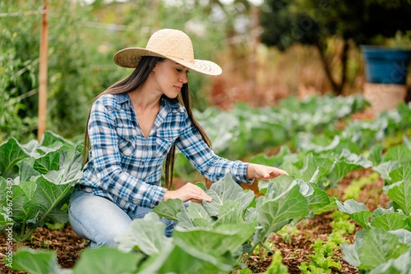 Fototapeta Young Woman in Straw Hat Tending Vegetable Garden Outdoors