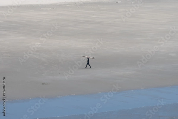 Fototapeta Surfer on empty beach carrying board over head