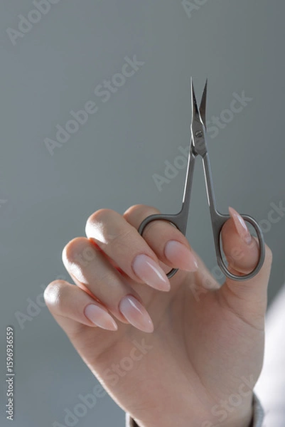 Fototapeta Manicure master's scissors in hand, showcasing perfect beige manicure in salon close-up