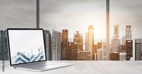 Obraz Laptop on table in office with panoramic sunset view of modern downtown skyscrapers at business district