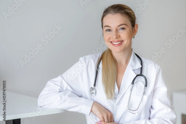 Fototapeta Smiling doctor in a white coat with a stethoscope in a modern office
