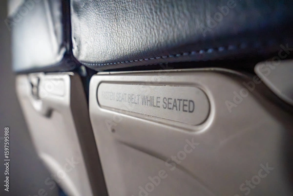 Fototapeta Close-up of seat sign on an airplane reading Fasten seat belt while seated. Air travel routine, safety instruction, and transportation awareness