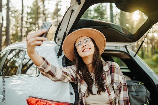 Obraz Young caucasian woman taking self portrait in scenic forest while sitting in car trunk