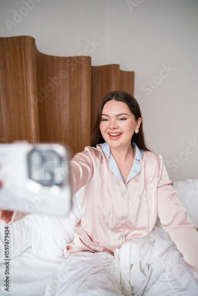 Obraz Joyful woman holding smartphone while sitting in bed