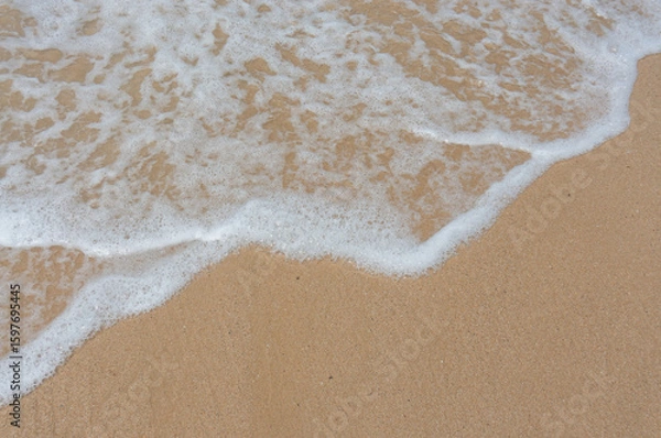 Fototapeta Soft wave on the sandy beach, background. View from the top of the sandy beach and foam from the wave.