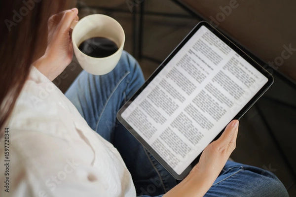 Fototapeta woman hand holding coffee cup and tablet, reading text on tablet device with a touchscreen interface for digital press article feed in the morning. mockup media publication website on portable tablet
