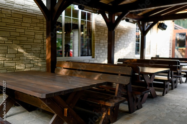 Fototapeta Wooden table and benches under a canopy, surrounded by greenery.