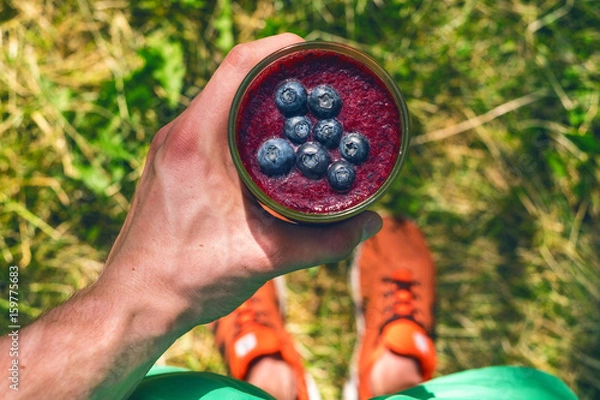 Fototapeta Smoothie drink a sport man in a nature. Glasses of smoothie with berry and mint. Berry, leaf and lime, raspberriesFruit Healthy food. Take a way breakfast.