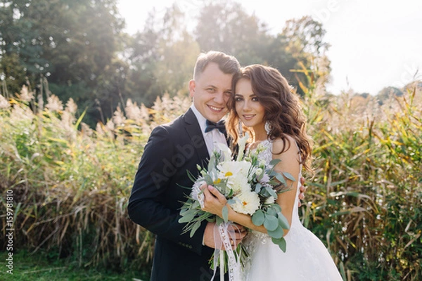 Fototapeta A nice, warm portrait of a stylish bridegroom and a charming bride in the nature