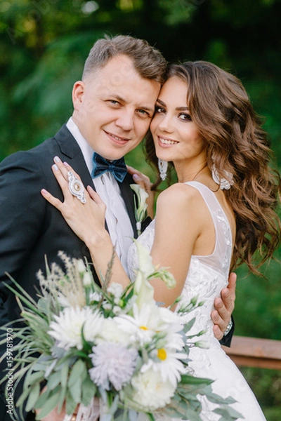 Fototapeta A nice, warm portrait of a stylish bridegroom and a charming bride in the nature