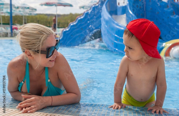 Obraz A mother in her 40's and a small child are communicating on the end of a pool in hot summer day