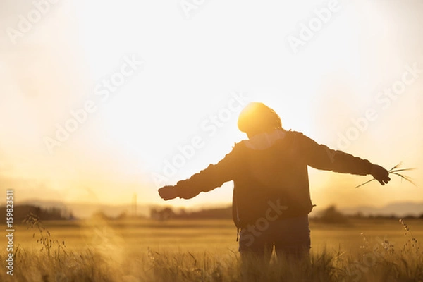 Fototapeta Middle aged caucasian woman standing in the sunlit field with open arms, embracing nature