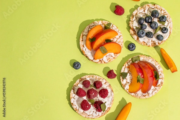 Obraz Rice cakes with different types garnish fruits, peaches, blueberries, apricots, raspberries with honey on green background. Healthy colorful food.