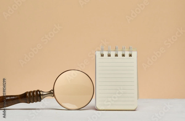 Fototapeta An open notebook with blank lined sheets of paper and a magnifying glass next to it. Searching for information, planning, analyzing or studying.