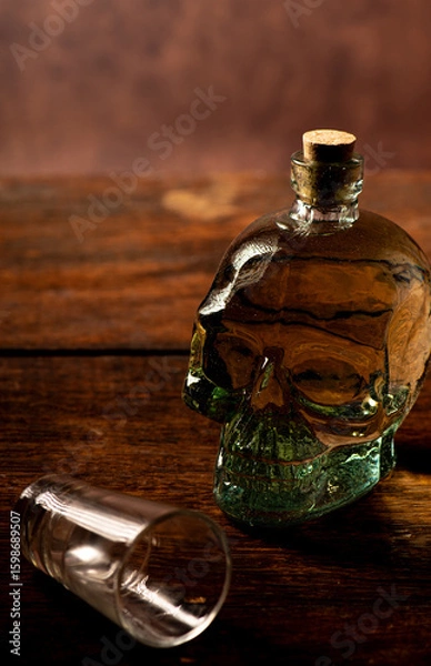 Obraz Cachaça, Brazilian cachaça bottle in the shape of a skull and a glass, on rustic wood and abstract background, low key photo, selective focus.