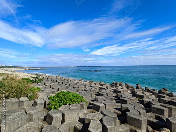 Fototapeta A beach half-filled with tetrapod and sandy at the other side facing the Pacific Ocean with a lighthouse in sight under a sunny blue sky during the pandemic