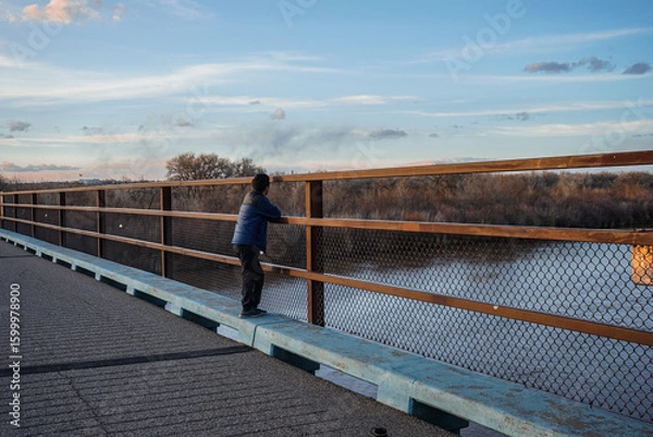 Fototapeta Man stands on bridge overlooking the Rio Grande River in Albuquerque, New Mexico, USA at sunset