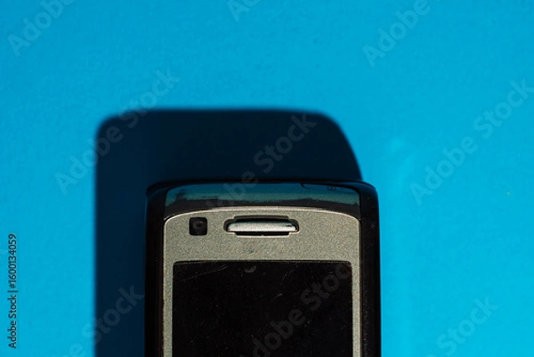 Fototapeta Top part of old mobile phone casting shadow on bright blue background. Bold retro composition. High quality photo