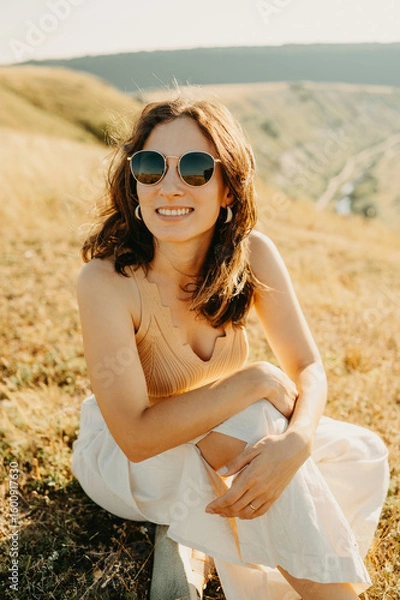 Obraz A joyful woman delighting in the warmth of the sun within a lush grassy landscape, celebrating natures beauty.