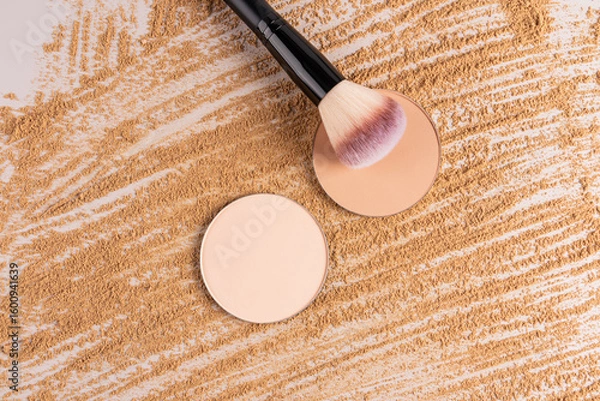 Obraz Two round blocks of compact powder refills in different tones lie on a beautiful background of spilled powder texture with a fluffy makeup brush.