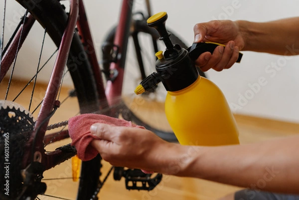 Fototapeta Detail cropped shot of unrecognizable man using yellow sprayer and cloth preparing to clean chain of mountain bike, emphasizing importance of bicycle maintenance after trail riding at home.