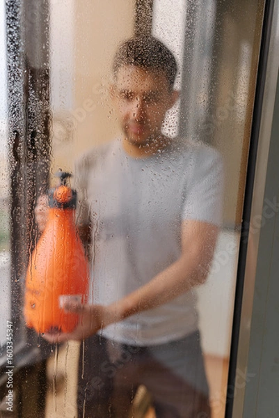 Fototapeta Blurred vertical portrait of homeowner cleaning solution onto large window in high-rise building, preparing to wipe away dirt and grime for sparkling clean finish. Concept of hygiene and cleanliness.