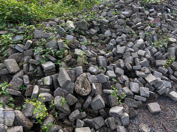 Fototapeta Pile of left over pavers, flooring or concrete block paving, cube shape, with green vines