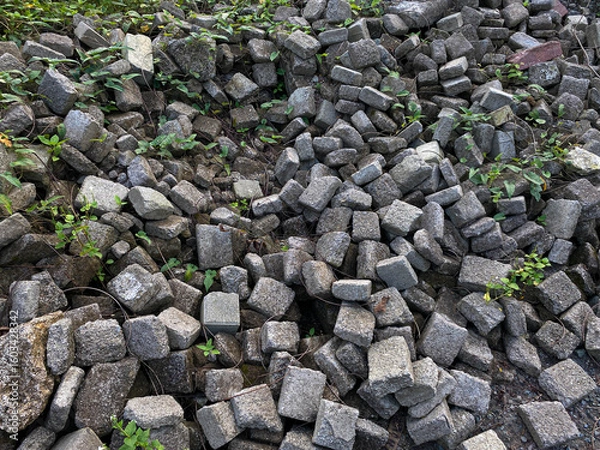 Fototapeta Pile of left over pavers, flooring or concrete block paving, cube shape, with green vines